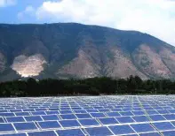 A large field of solar panels with mountains in the background.