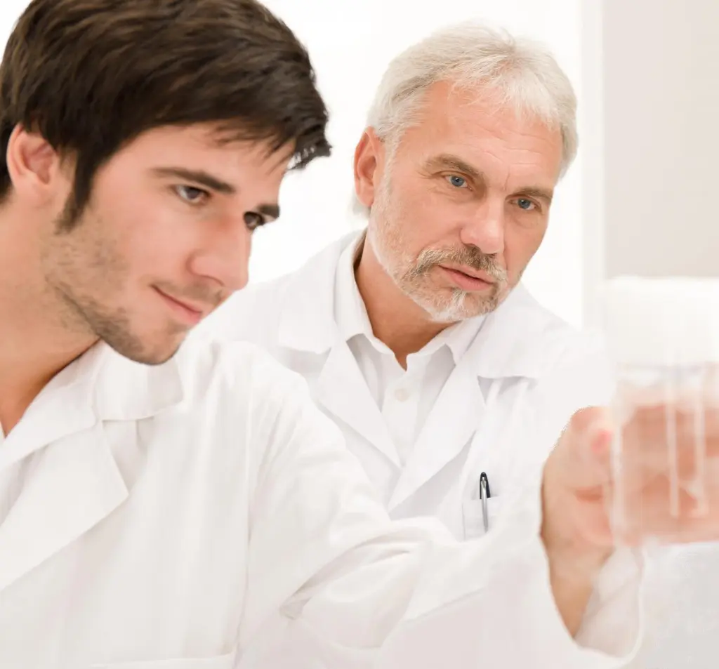Two men in lab coats looking at a glass.