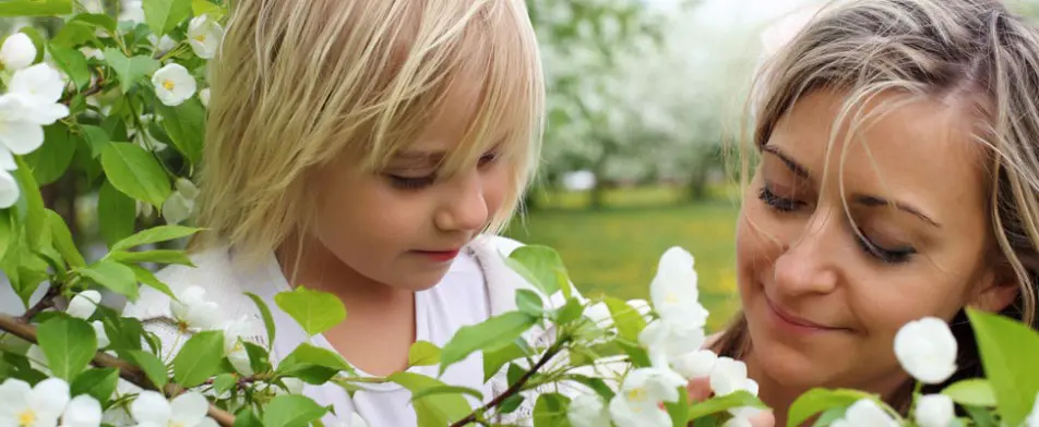 A little girl looking at flowers in the grass.
