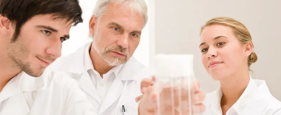 A man in white lab coat holding a glass.